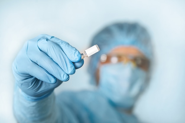 Close up van dokter hand met vaccin. Medische uitrusting. Een arts die persoonlijke beschermingsmiddelen draagt, waaronder een masker, bril en pak om de COVID 19-coronavirusinfectie te beschermen.