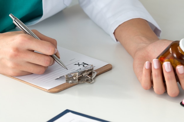 Close-up van doktershanden die voorschrift schrijven en fles met pillen houden. Gezondheidszorg, medisch en apotheekconcept.