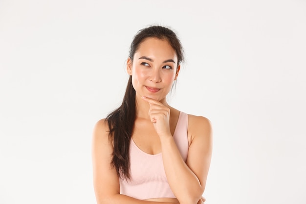 Close-up van doordachte Aziatische fitness meisje, vrouwelijke atleet plan maken, sluwe linker bovenhoek kijken terwijl nadenken, iets kiezen.