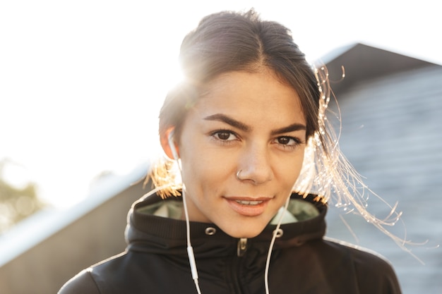 Close up van een aantrekkelijke jonge fitness vrouw, gekleed in sportkleding buitenshuis oefenen, luisteren naar muziek met koptelefoon