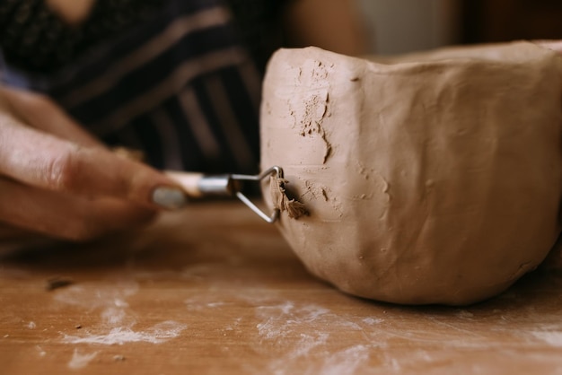 Close-up van een aardewerken kom en vrouwelijke handen versieren een keramisch product met een speciaal gereedschap Potter's creatieve workshop handwerkconcept