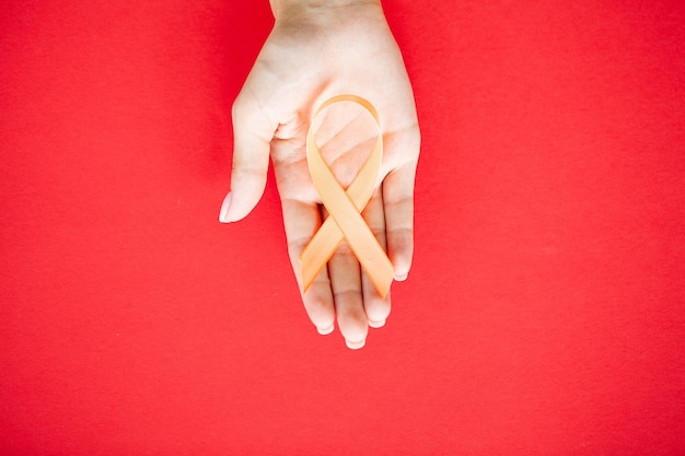 Close-up van een arts die oranje bewustzijnslint in haar handen vasthoudt en toont