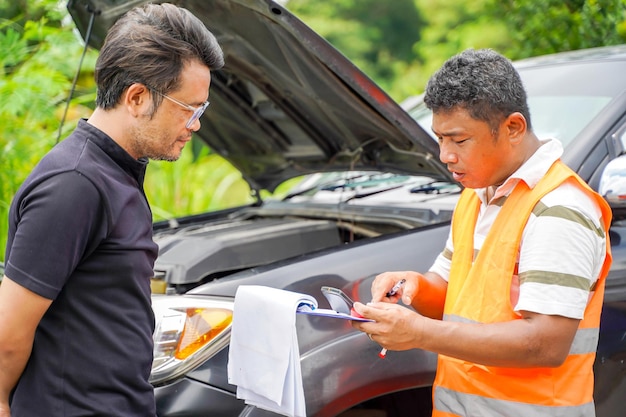 Close-up van een auto-mechanicus die op een klembord schrijft terwijl hij een auto onderzoekt na het beoordelen van een ongevallenclaim