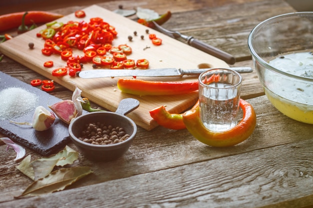 Foto close-up van een azijnglas en hele peper naast een bord met gehakte chili pepers op een oude houten oppervlak