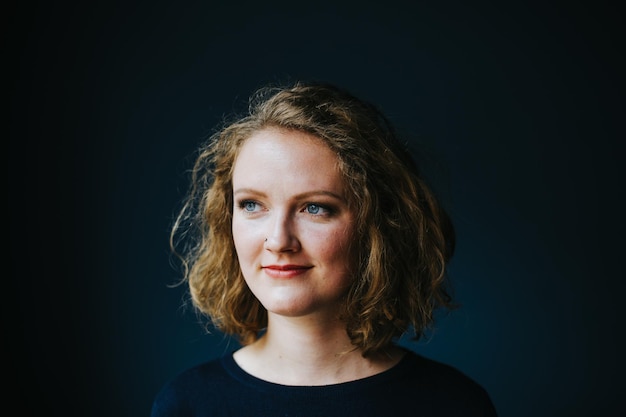 Close-up van een bedachtzame vrouw die glimlacht terwijl ze wegkijkt tegen de muur