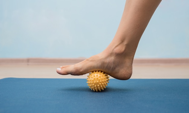 Close-up van een been dat een gele massagebal op een mat rolt
