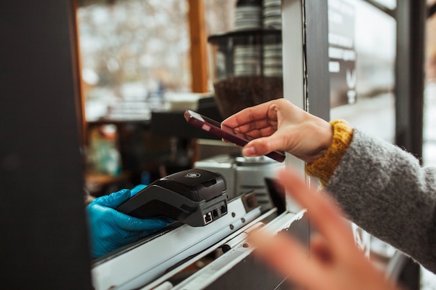 Close-up van een betaalterminal en een mobiele telefoon in handen van de vrouw die voor koffie betalen.