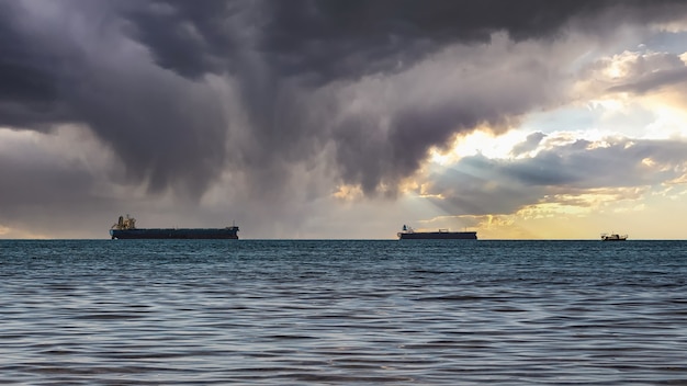 Foto close-up van een bewolkt zeegezicht en een heldere zonsondergang. blauwe zee, onweerswolken met zonnestralen aan de horizon en verschillende vrachtschepen.