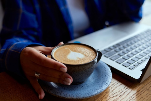 Close-up van een blank meisje dat op een toetsenbord schrijft naast een kop koffie