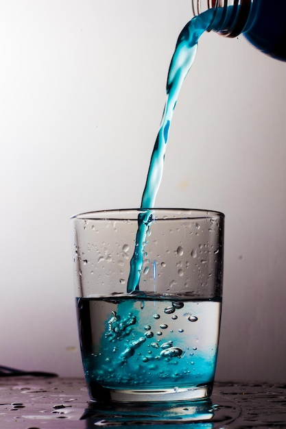 Foto close-up van een blauwe drank die in een glas wordt gegoten tegen een witte achtergrond