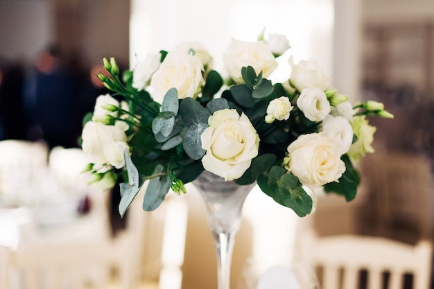 Close-up van een boeket van witte rozen in transparante vaas bij een huwelijksreceptie