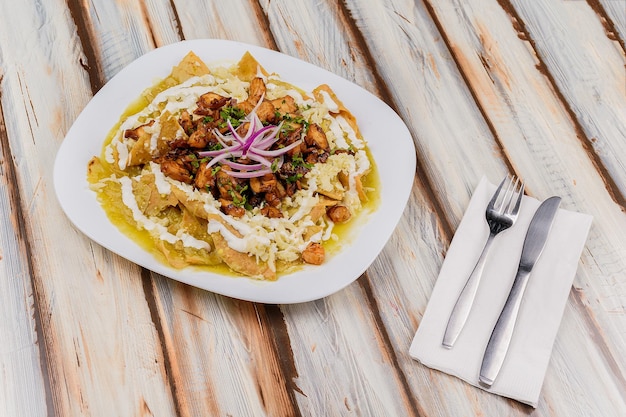 Close-up van een bord met chilaquiles in veracruz-stijl met groene saus op een tafel