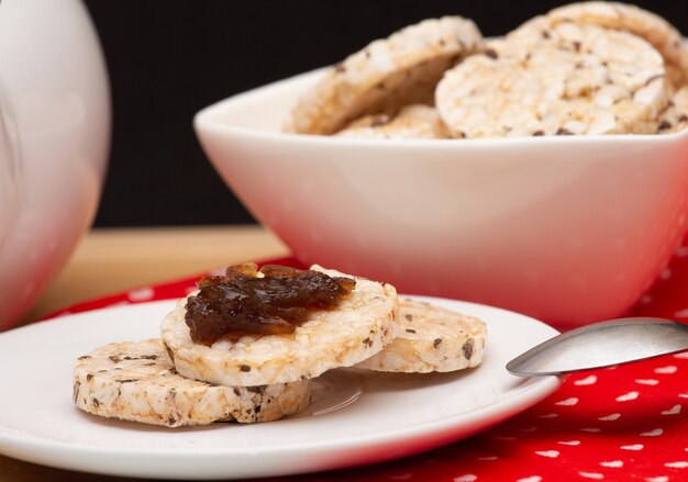 Close-up van een bord met veganistische rijstkoekjes met gelei bovenop naast een kom vol rijstkoekjes