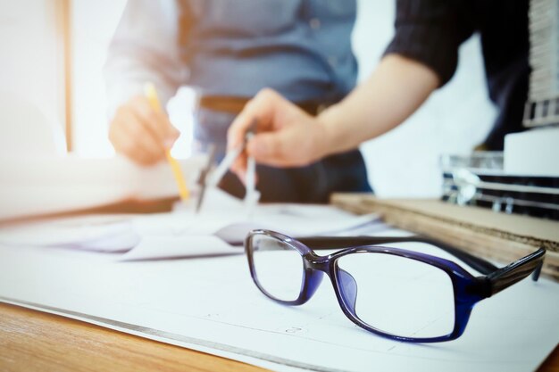 Close-up van een bril tegenover collega's die aan een blauwdruk werken
