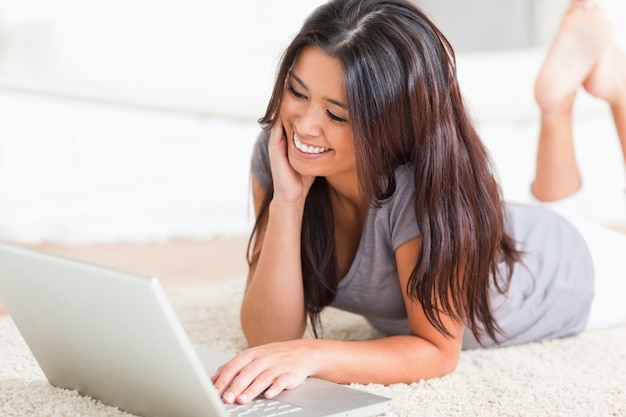 close-up van een charmante vrouw liggend op een tapijt met een notebook