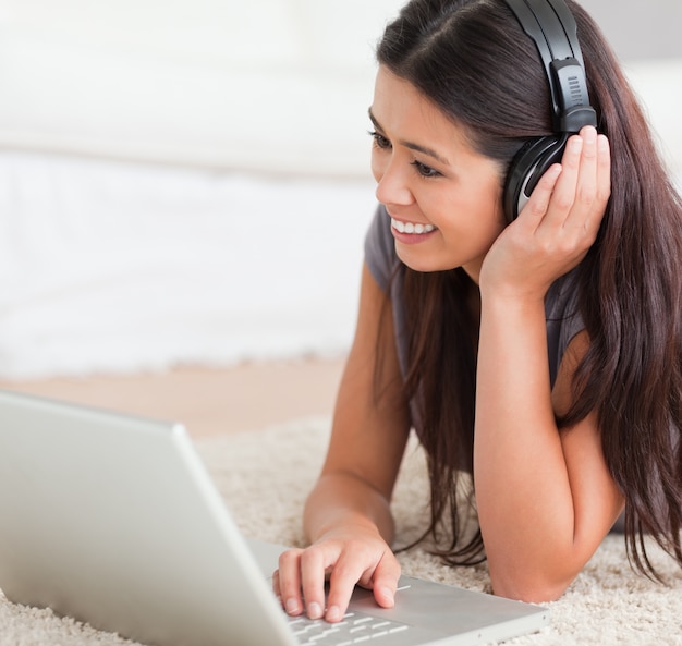 close-up van een charmante vrouw liggend op een tapijt met laptop en oortelefoons