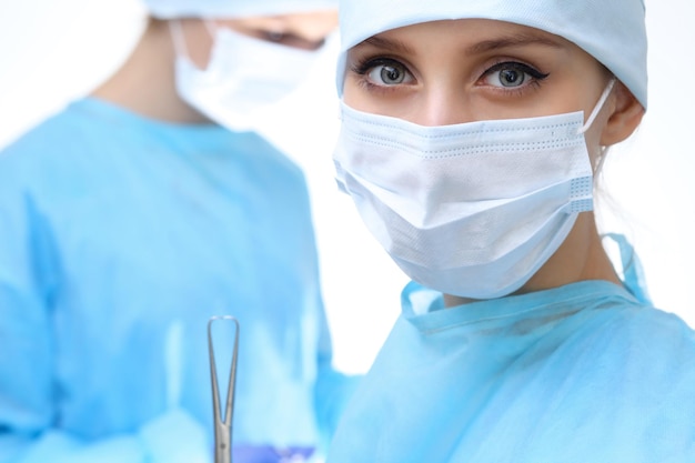 Close-up van een chirurg vrouw die naar de camera kijkt terwijl collega's op de achtergrond optreden in de operatiekamer, geïsoleerd. Chirurgie en geneeskunde concept