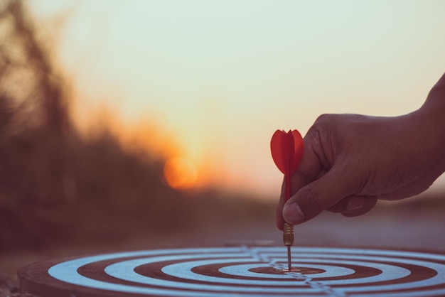 Foto close-up van een dart met de hand op het dartbord tegen de hemel tijdens de zonsondergang