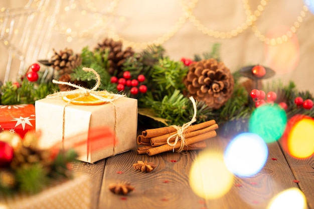 Close-up van een doos met een geschenk verpakt in kraftpapier en een kerstachtergrond met een kerstboom versierd met decoratieve ballen met gouden lampjes op een houten tafel kaneelstokjes kopieer ruimte