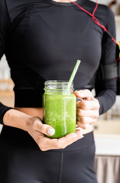 Close up van een fit vrouw in zwarte sportkleding met een potje groene smoothie