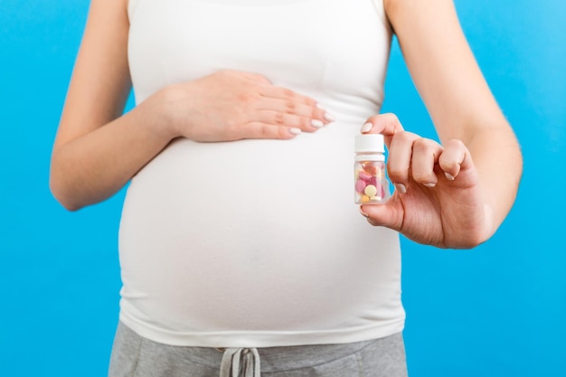 Close-up van een fles vitaminepillen in de hand van de zwangere vrouw op een kleurrijke achtergrond met kopieerruimte Gezondheidszorgconcept