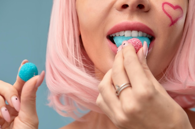 Close up van een flirterig vrouwelijk model op blauwe achtergrond, het dragen van een roze pruik met een snoepje in de mond Vrij glamoureuze vrouw roze haar charme snoep levensstijl genot suiker
