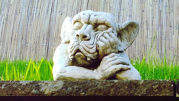 Foto close-up van een gargoyle standbeeld tegen een bamboe hek