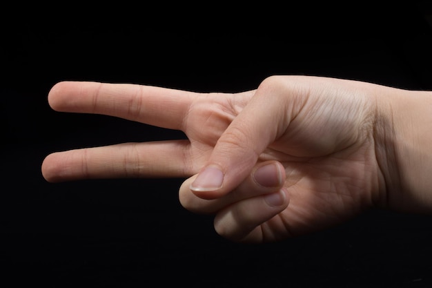 Close-up van een gekapte hand met een vredesteken op een zwarte achtergrond