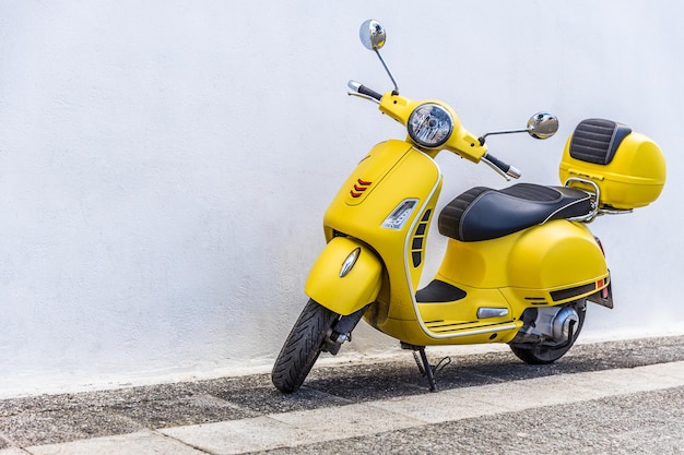 Close-up van een gele Vespa Piaggio-scooter geparkeerd in een straat met een witte muur, een oude versierde straat