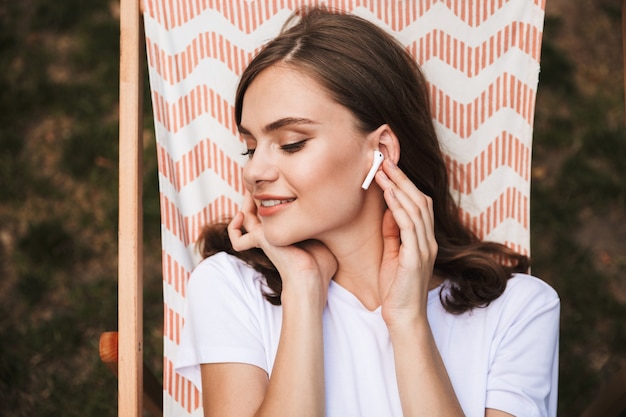 Close up van een gelukkig jong meisje, luisteren naar muziek met oortelefoons tijdens het rusten op een hangmat in het stadspark buiten in de zomer