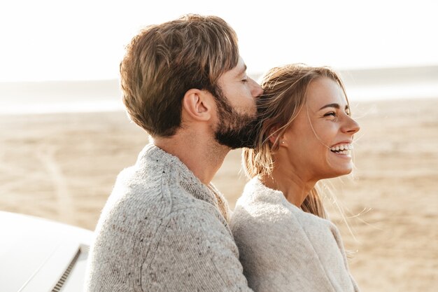 Close up van een gelukkig jong verliefd stel omarmen terwijl leunend op een auto op het zonnige strand