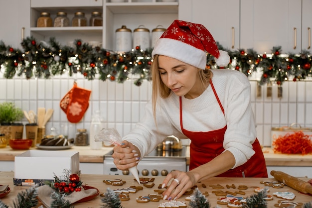 Close-up van een gelukkige moeder met een rode schort die kerstkoekjes decoreert met poedersuiker in de keuken