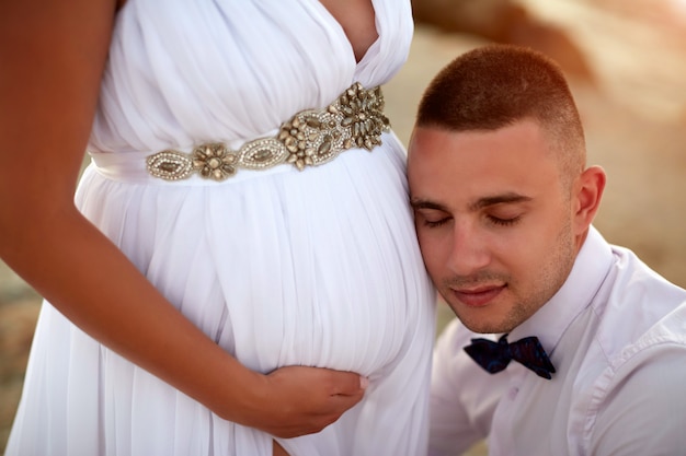Close-up van een gelukkige toekomstige vader die aan buik van zijn zwangere vrouw luistert