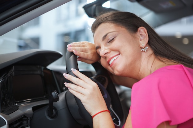 Close-up van een gelukkige vrouw die het stuur van haar auto knuffelt, glimlachend met gesloten ogen