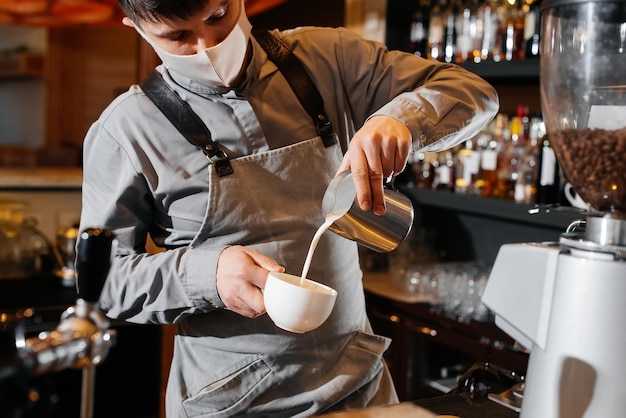 Close-up van een gemaskerde bartista die heerlijke heerlijke koffie bereidt aan de bar in een coffeeshop Het werk van restaurants en cafés tijdens de pandemie