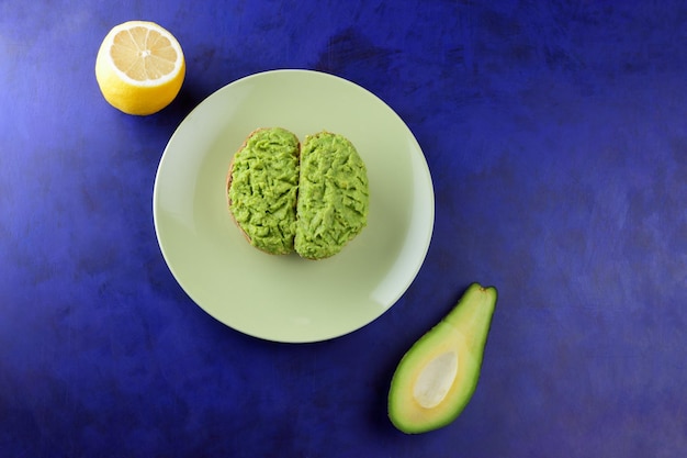 Close-up van een gezonde snack eten op een blauwe achtergrond Twee vegetarische toast met avocado en citroen op een groene plaat View from above