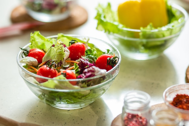 Close-up van een glazen kom met verse kool en tomatensalade staande op de tafel met andere kommen in de buurt