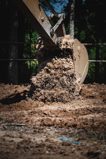 Close-up van een graaflaadmachine die restjes en grond uit de grond plukt door grond te graven voor constructie tijdens een heldere en zonnige dag met water dat eruit spat