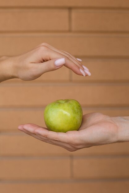 Close-up van een groene appel die in de palm van een man ligt terwijl de hand van een vrouw hem van bovenaf bedekt