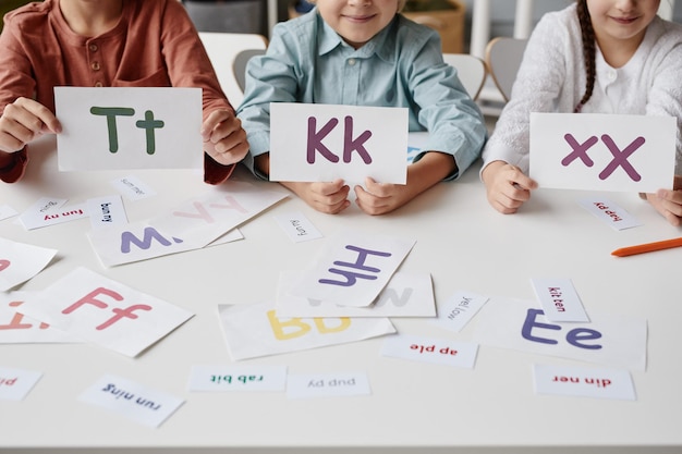 Close-up van een groep kinderen die met kaarten aan de tafel spelen, ze leren in het Engels te lezen