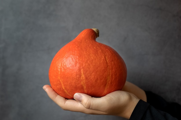 Close-up van een halloween-pompoen in handen van vrouwen tegen een idee van een donkere achtergrond