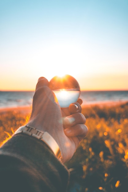 Foto close-up van een hand die een kristallen bol vasthoudt tegen de hemel tijdens de zonsondergang