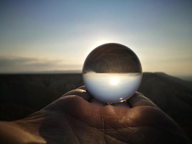 Foto close-up van een hand die een kristallen bol vasthoudt tegen de hemel tijdens de zonsondergang