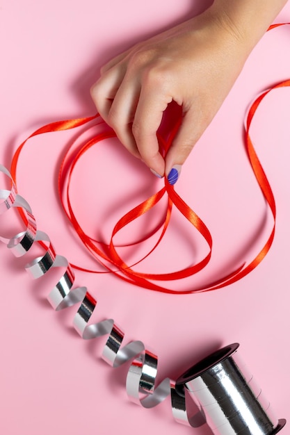 Close-up van een hand die een lint vasthoudt voor het verpakken van geschenken op een roze achtergrond