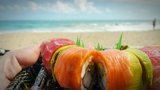 Foto close-up van een hand die een sushiplaat tegen de zee vasthoudt