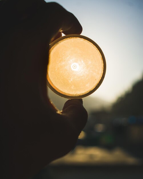 Close-up van een hand die een verlichte gloeilamp vasthoudt tegen de hemel tijdens de zonsondergang