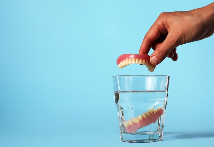 Close-up van een hand die kunsttanden in een waterglas stopt