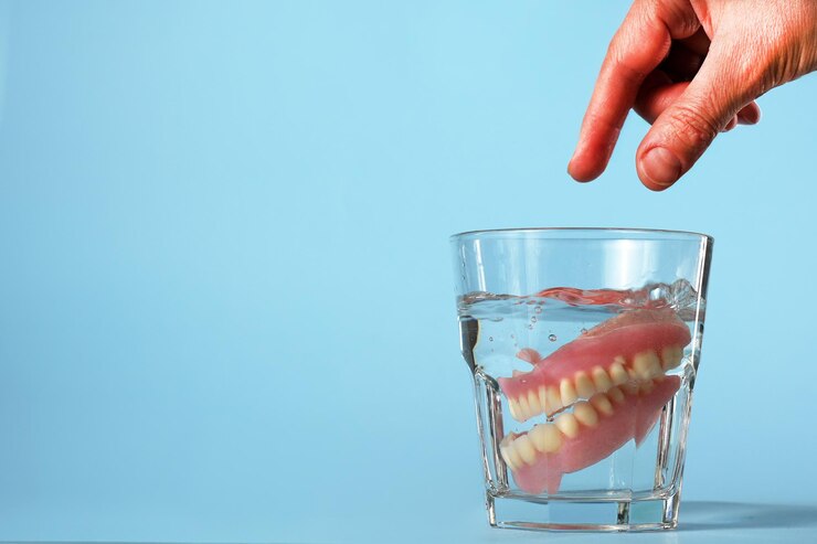 Close-up van een hand die kunsttanden in een waterglas stopt