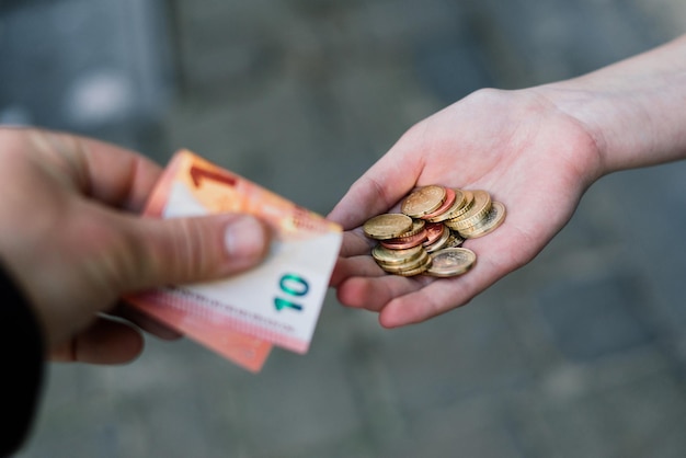Close-up van een hand die munten aan een andere hand geeft met bankbiljetten