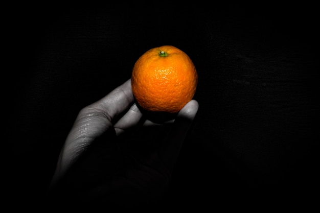 Close-up van een hand die oranje vasthoudt op een zwarte achtergrond